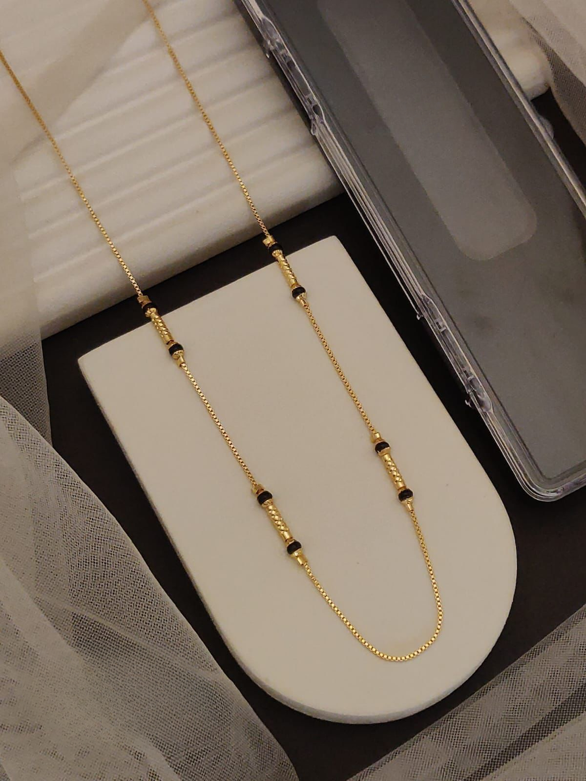 Gold necklace with black beads on a white surface