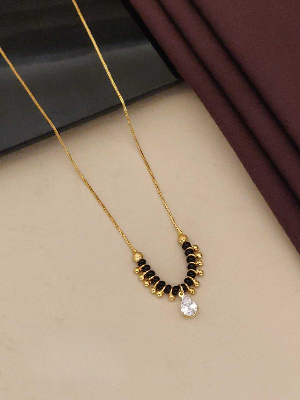 Gold and black beaded necklace with a clear gemstone on a beige surface.