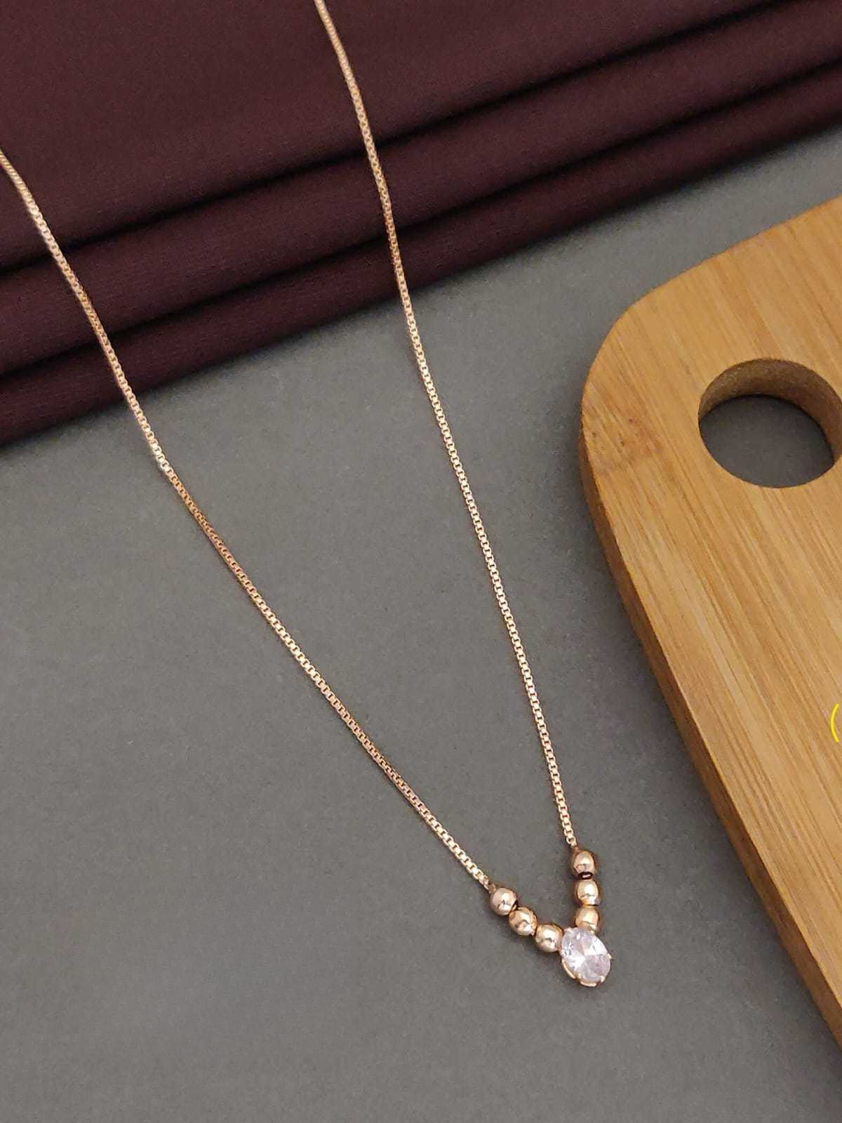 Delicate gold necklace with a clear gemstone on a gray surface with a wooden board in the background