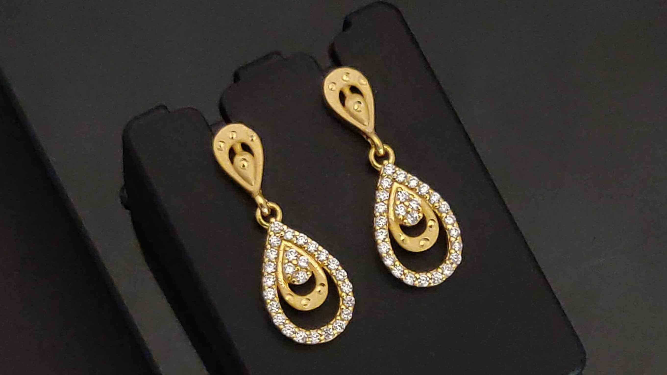 Gold teardrop earrings with diamond accents on a black background