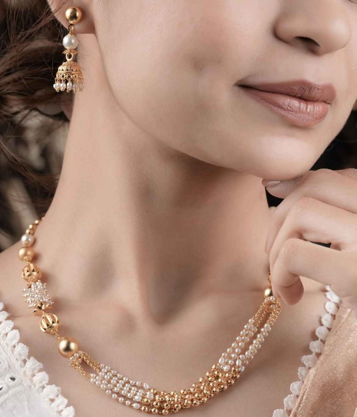 Close-up of a woman wearing a gold and pearl necklace and earrings.