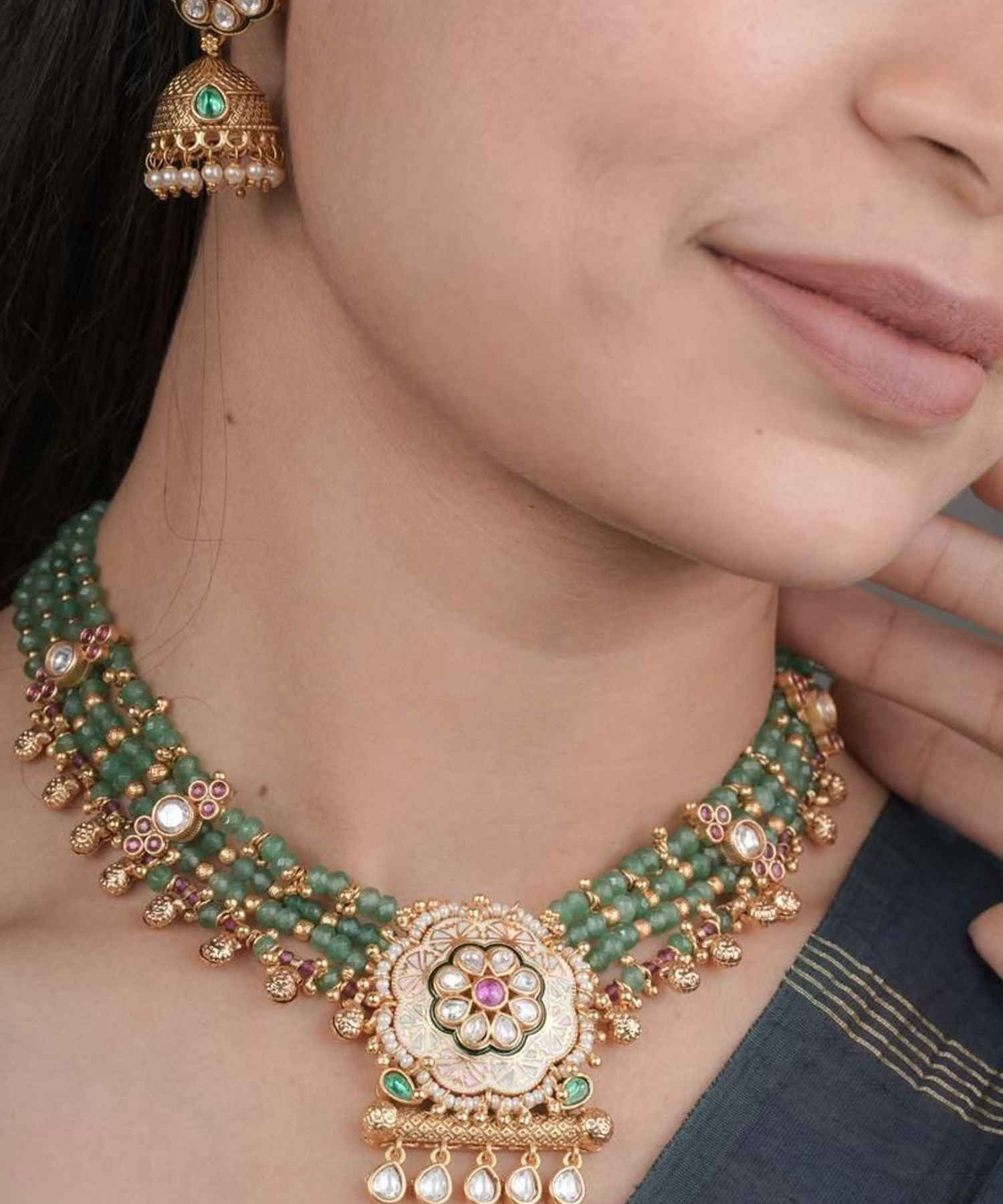 Close-up of a person wearing a green and gold necklace with matching earrings.
