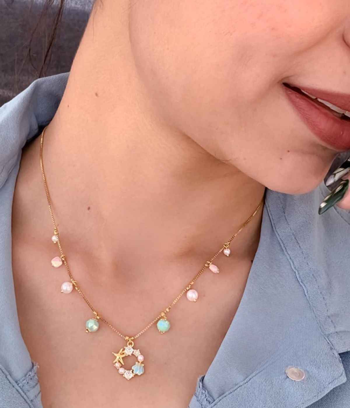 Necklace with starfish and heart pendants worn by a person in a blue shirt.