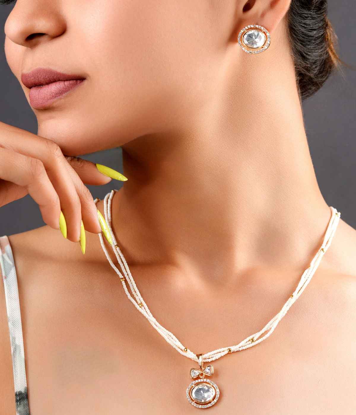Close-up of a woman wearing a gold necklace and earrings with a neutral background