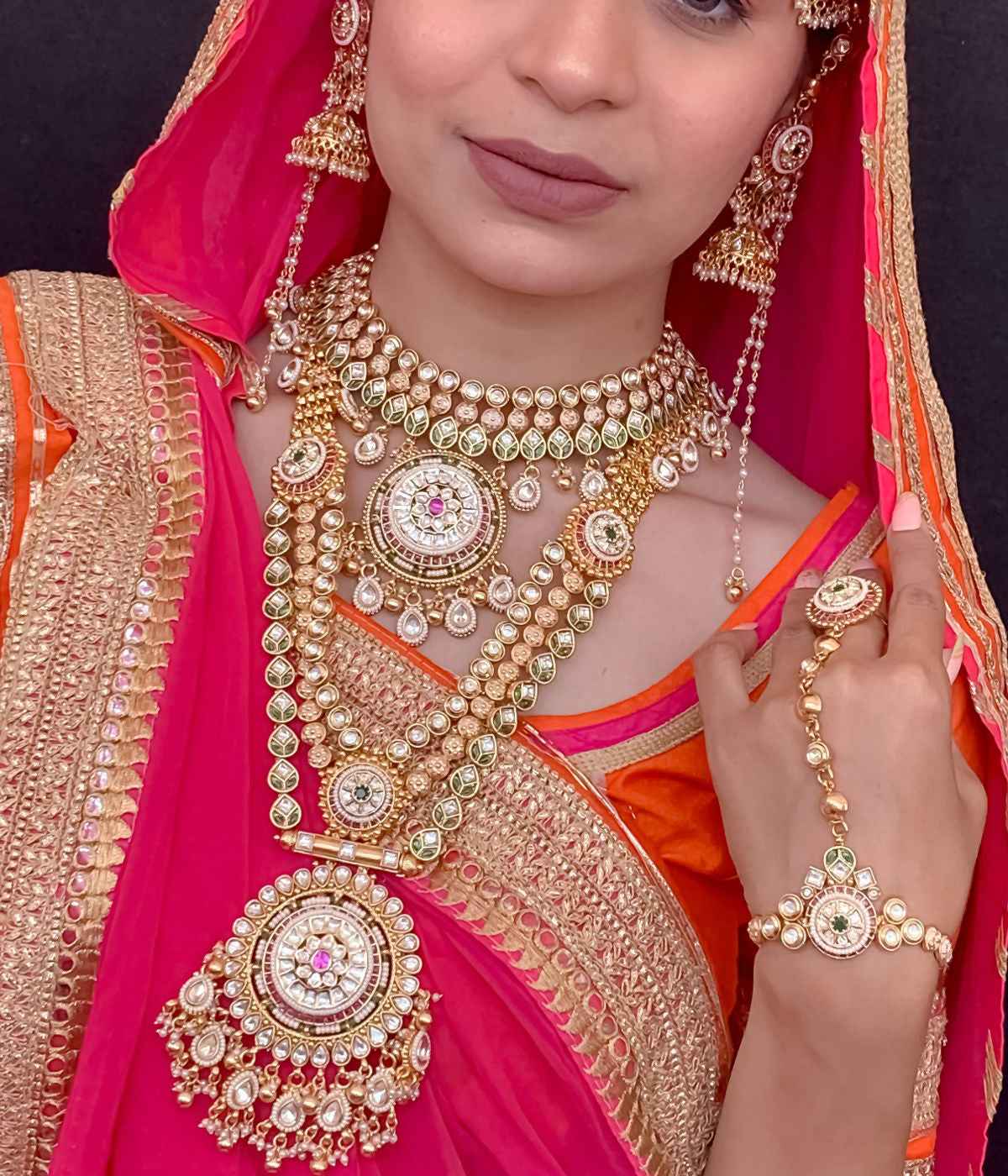 Woman wearing traditional Indian jewelry and attire with a bright pink and orange saree.
