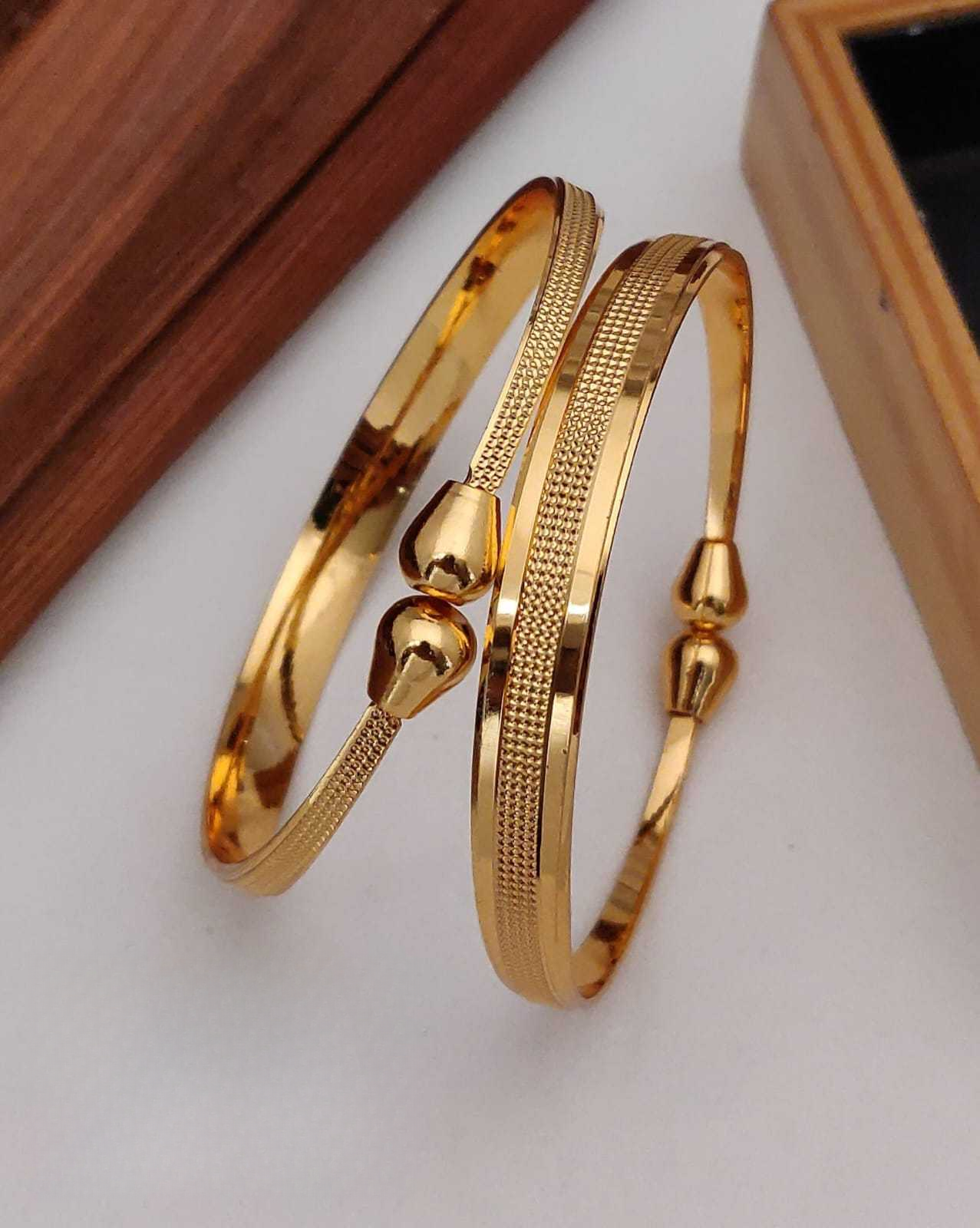 Two gold bangles on a white surface with a wooden box in the background.