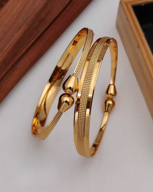 Two gold bangles on a white surface with a wooden box in the background.