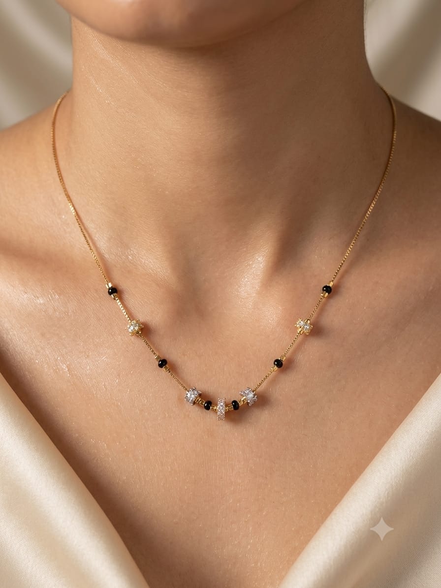 A delicate gold chain necklace with small black beads and clear crystal flower-like accents, worn on a model's neck against a soft cream satin background.