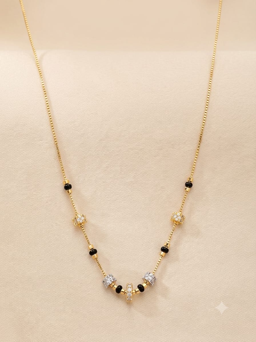 A delicate gold chain necklace with small black beads and a central cluster of clear and gold-toned stones, displayed on a soft beige jewelry stand.