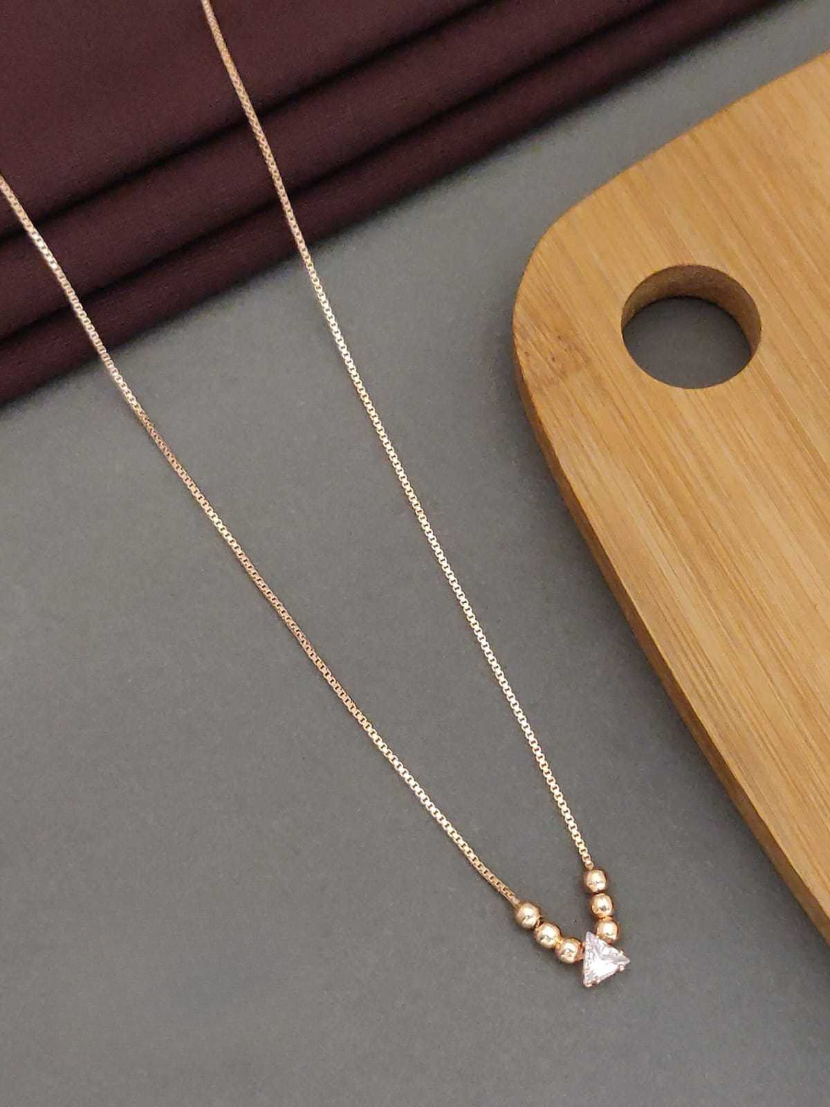 Gold necklace with a small diamond pendant on a gray surface with a wooden board in the background