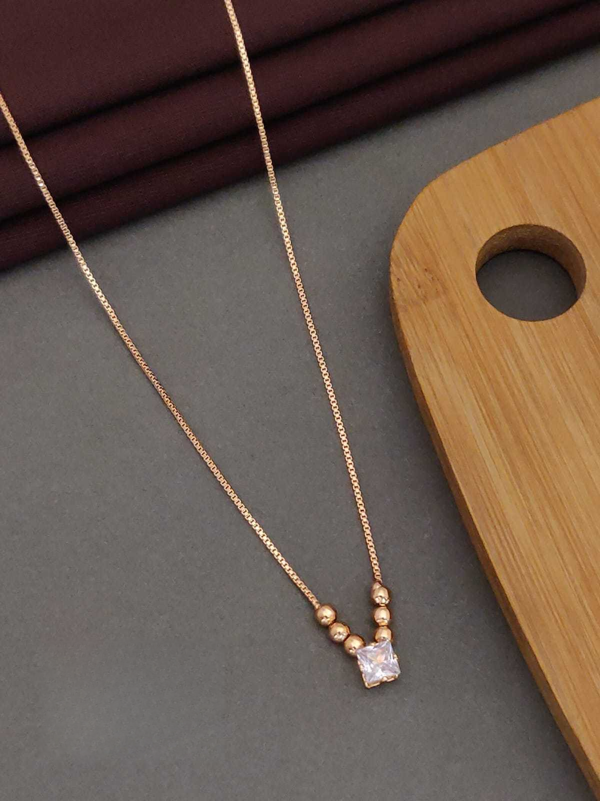 Rose gold necklace with a square pendant on a gray surface with a wooden block.