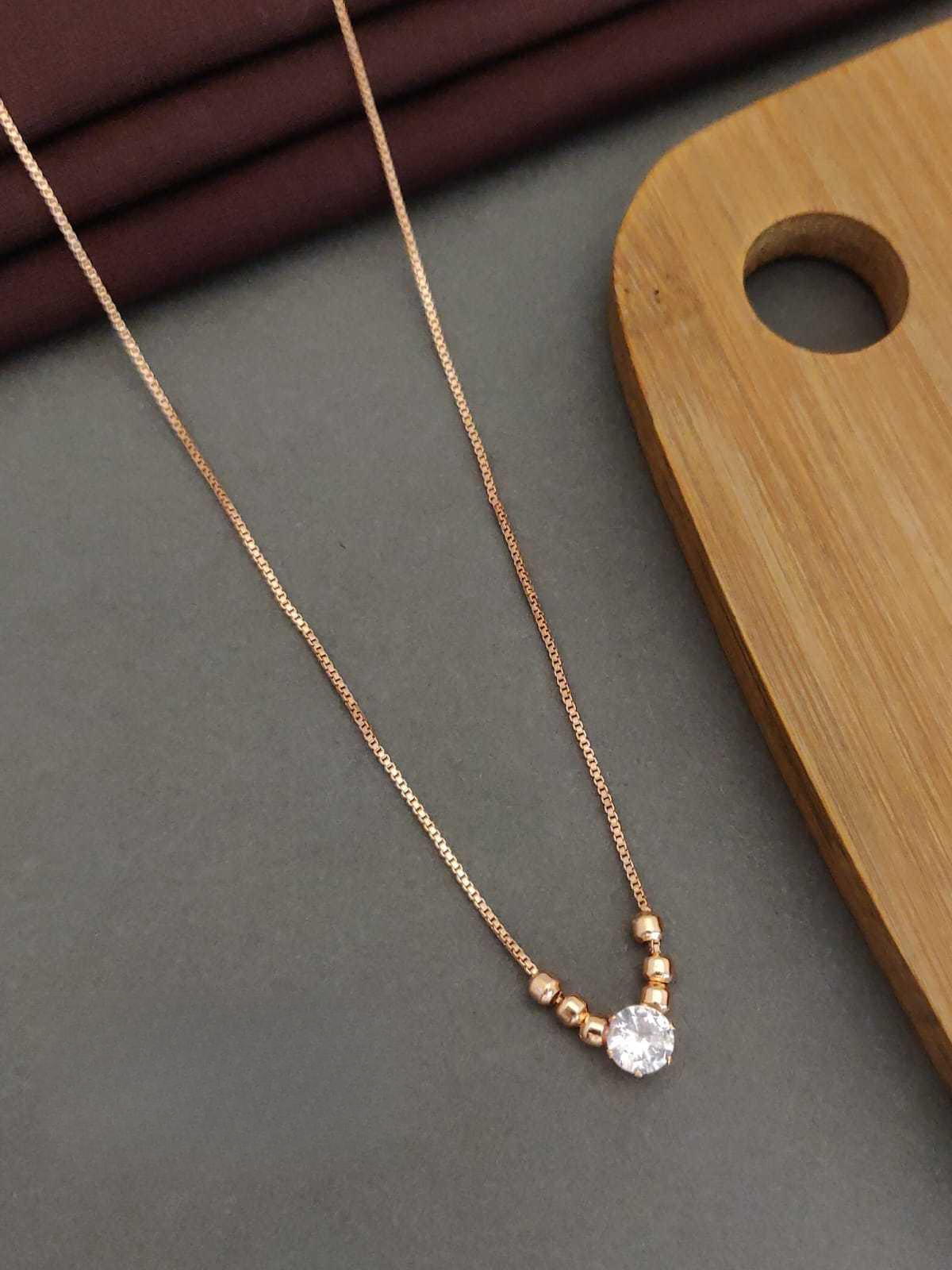 Rose gold necklace with a single crystal pendant on a gray surface with a wooden board in the background