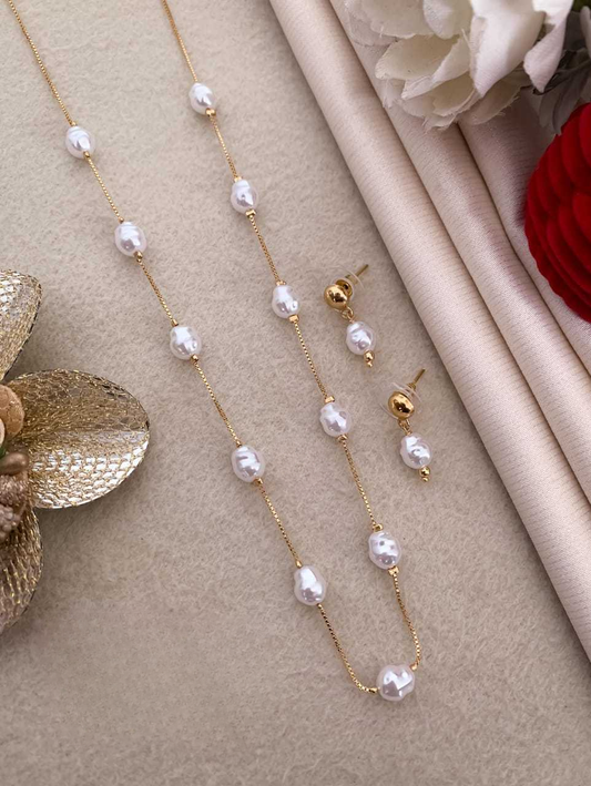 Pearl necklace and earrings on a beige surface with flowers in the background