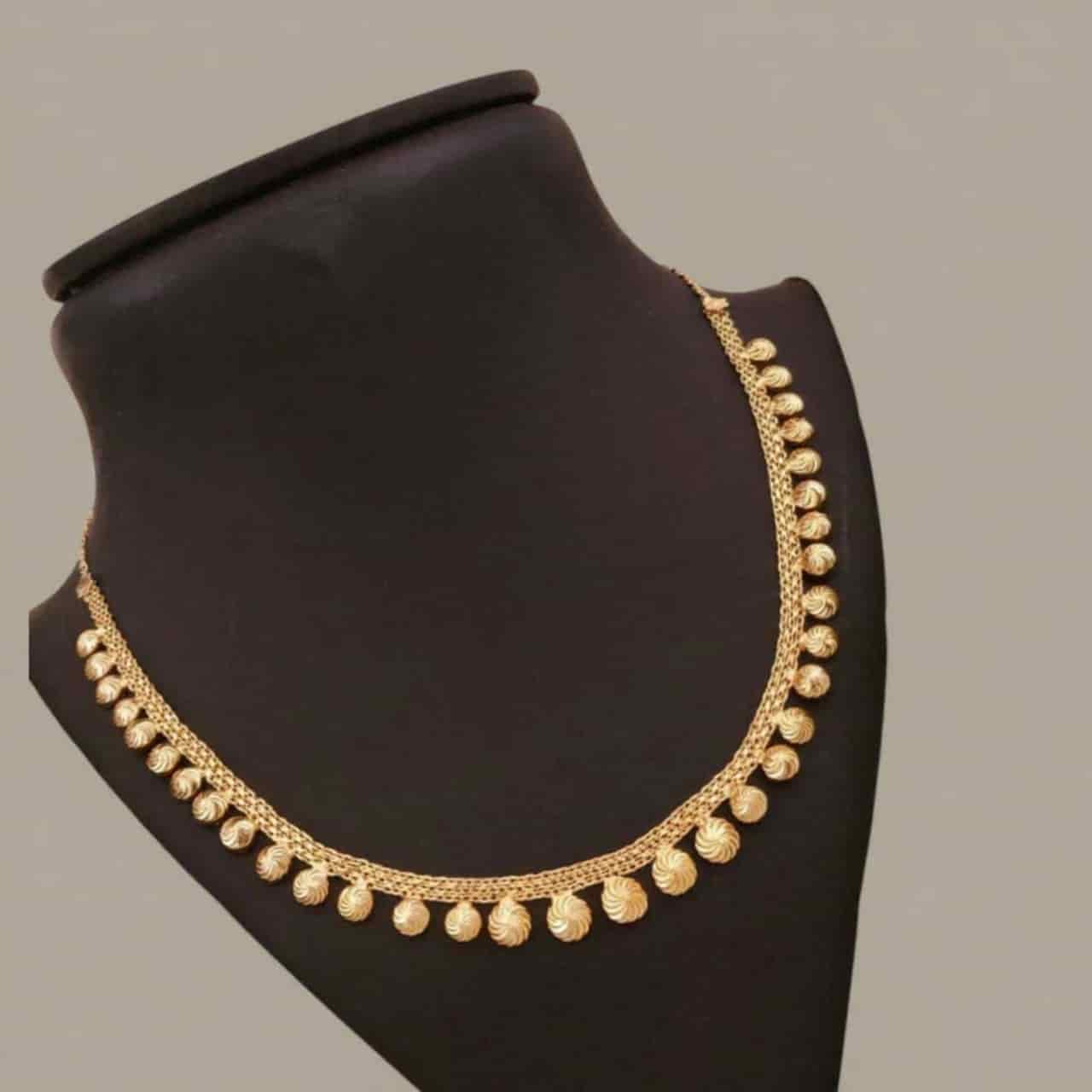Gold necklace on a black mannequin bust against a gray background
